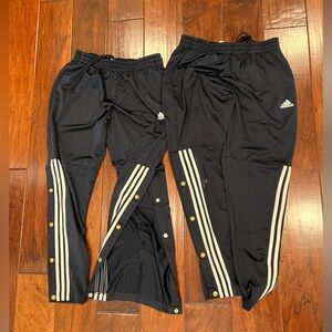 Two men’s adidas long pants with button openings on the bottom.